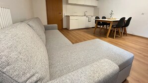 A modern living room with a grey sofa, a dining table with chairs, and a kitchen area with white cabinets. - Friendly warm apartment between Alb and Rems incl. sauna (Böbingen)