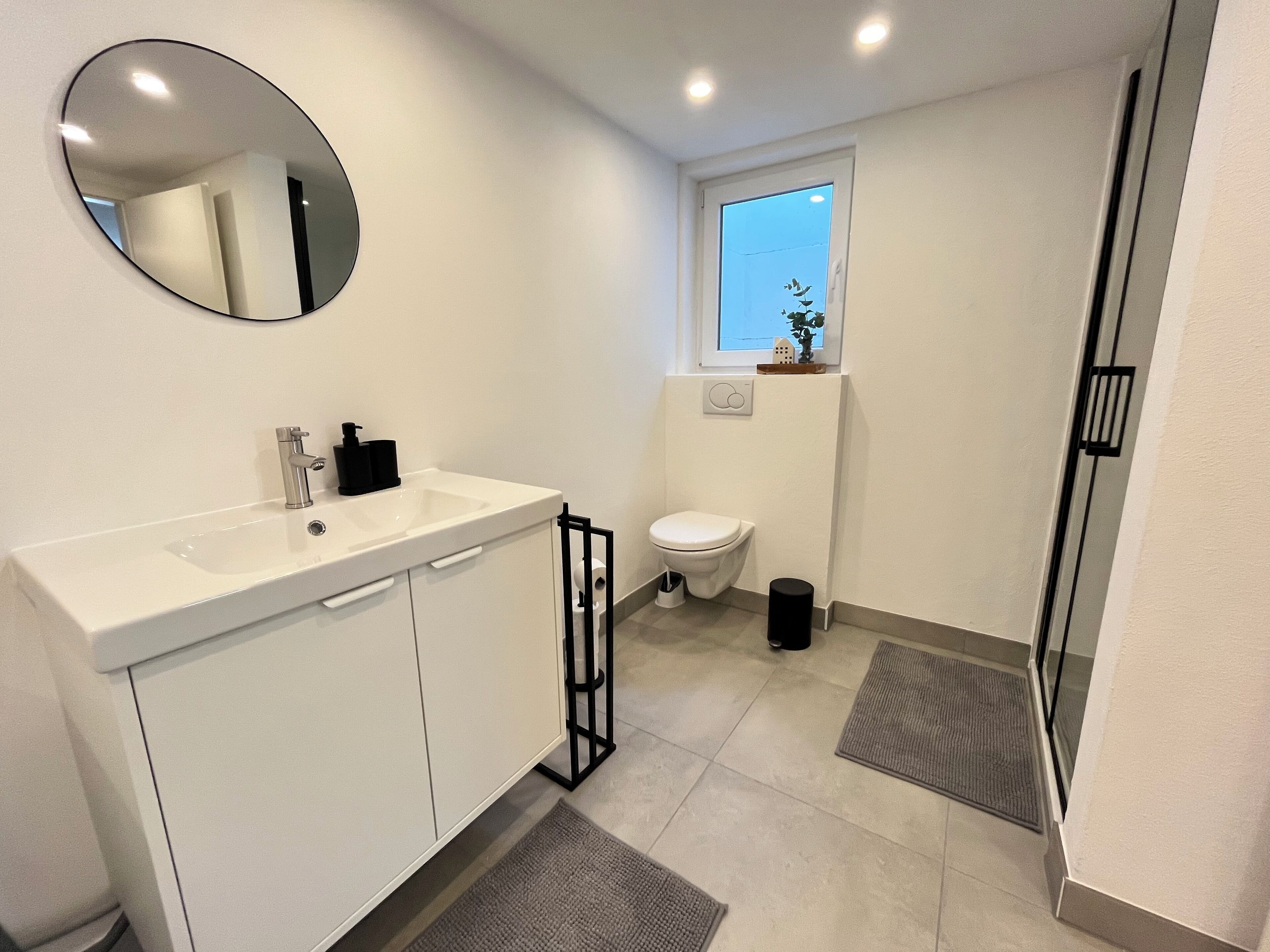 A modern bathroom with a white sink, mirror, and toilet.