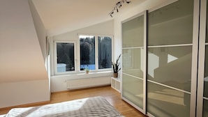 Un dormitorio con techo inclinado, ventanas amplias, una cama y un cerramiento de vidrio corredero.
