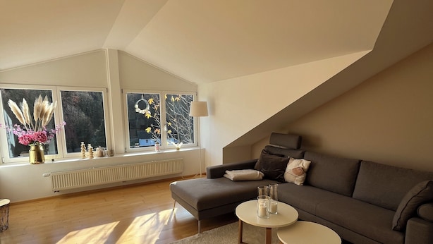 Una sala de estar moderna tipo loft, con techo alto, ventanas amplias, un sofá gris, dos mesas redondas de centro y una alfombra blanca.