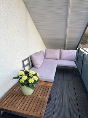 A balcony with a wooden table, a cushioned seating area, and a potted plant.