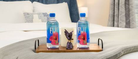 A bed with pillows, a bedside table with two bottles of Fiji water, and a small decorative item.