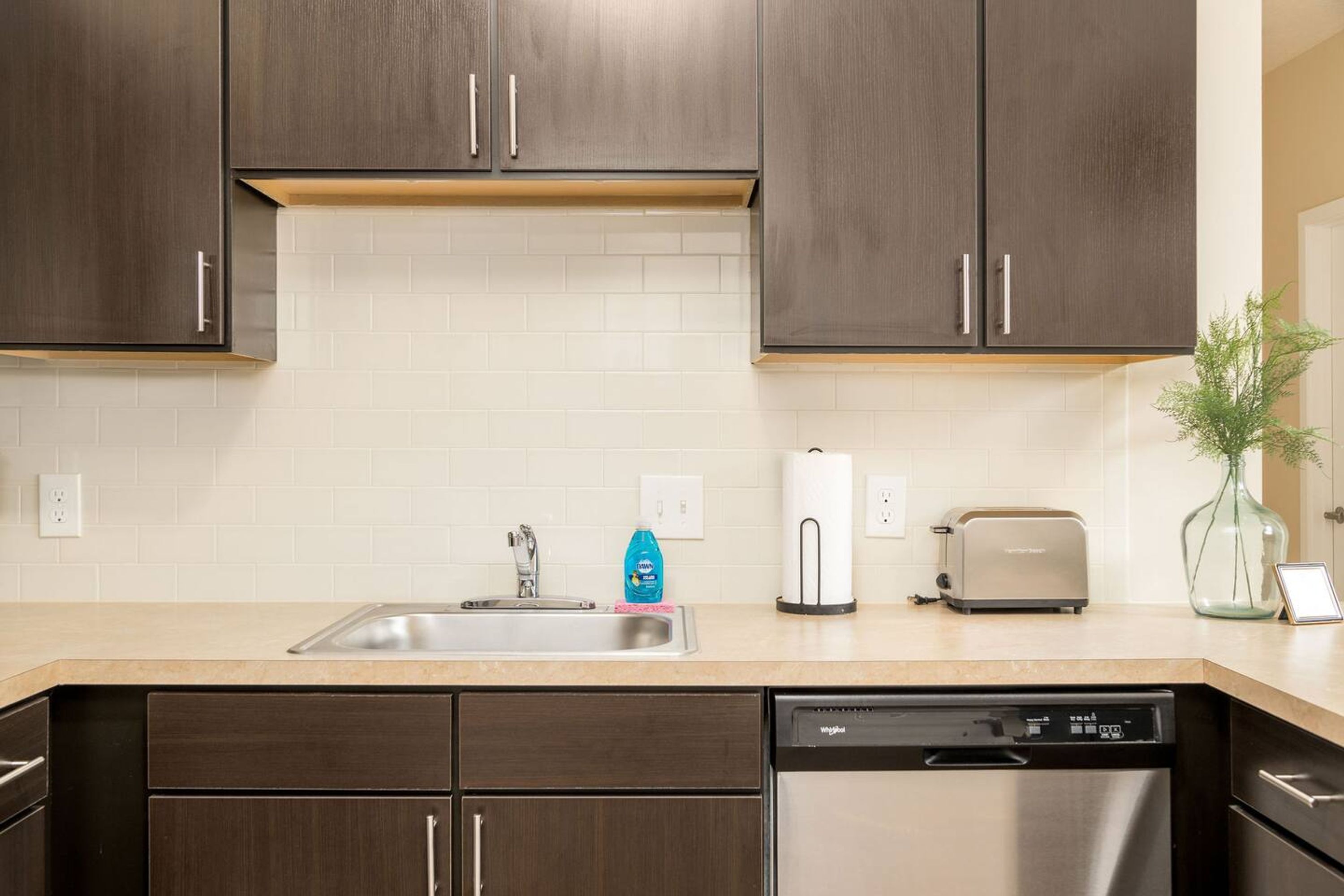 Una cocina moderna con armarios de madera oscura, un lavavajillas de acero inoxidable y un tostador sobre la encimera.