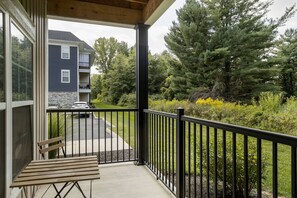 A balcony with a wooden table and a black railing overlooking a driveway and a building with a stone facade.