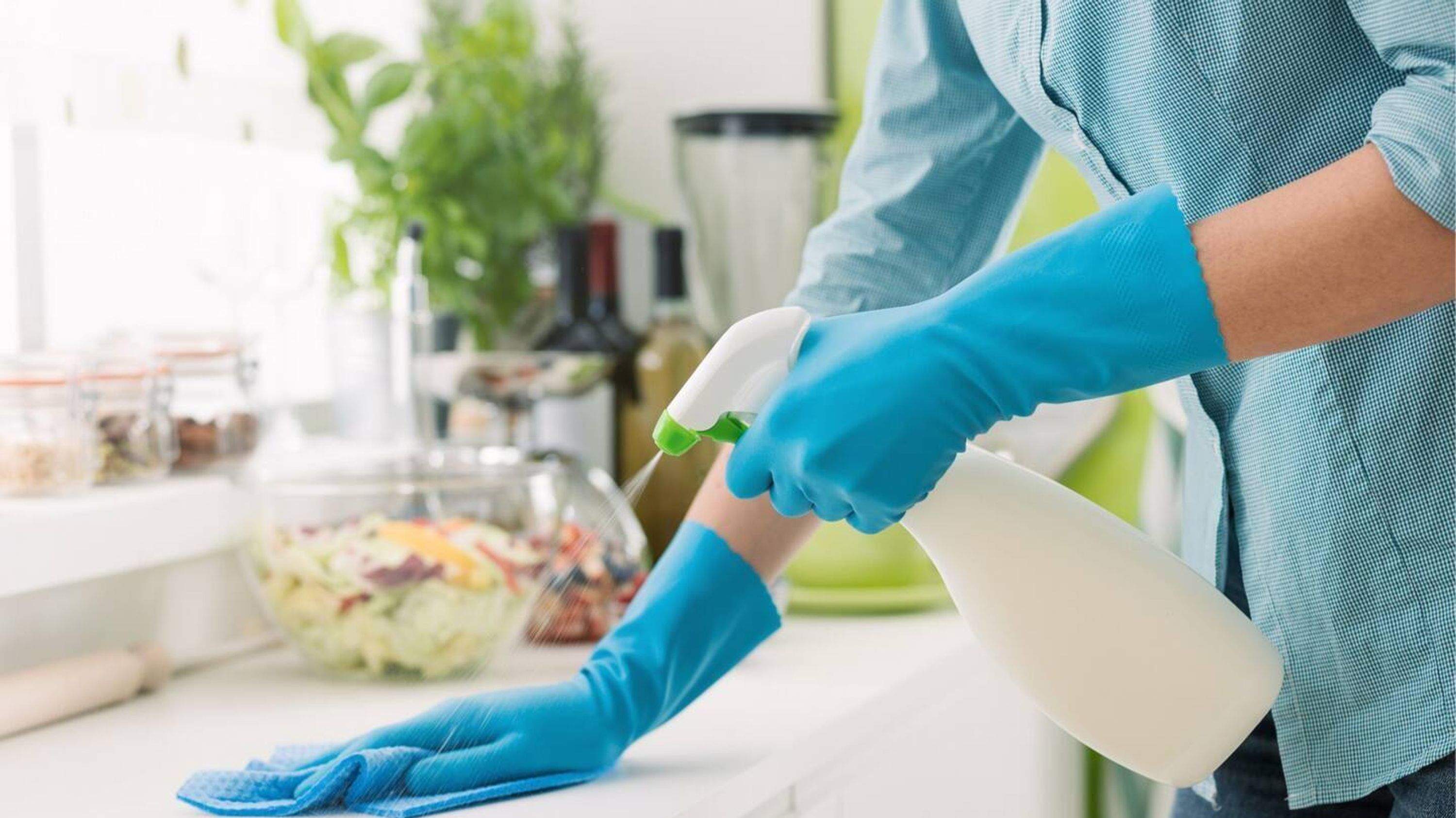Une personne portant des gants bleus nettoie un comptoir à l’aide d’un vaporisateur contenant un produit désinfectant.