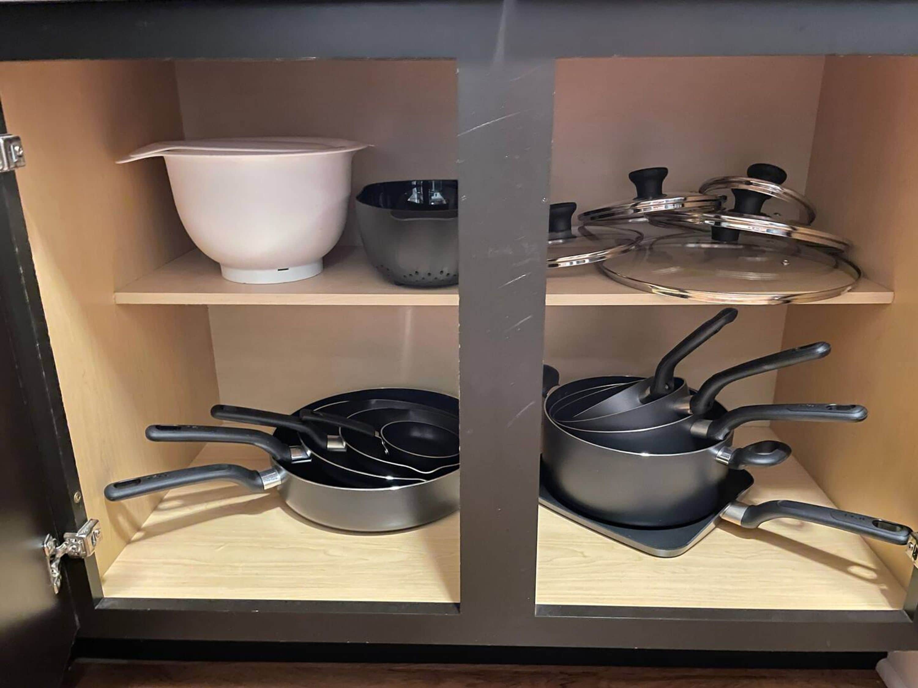 A kitchen cabinet with shelves holding cookware and kitchenware.