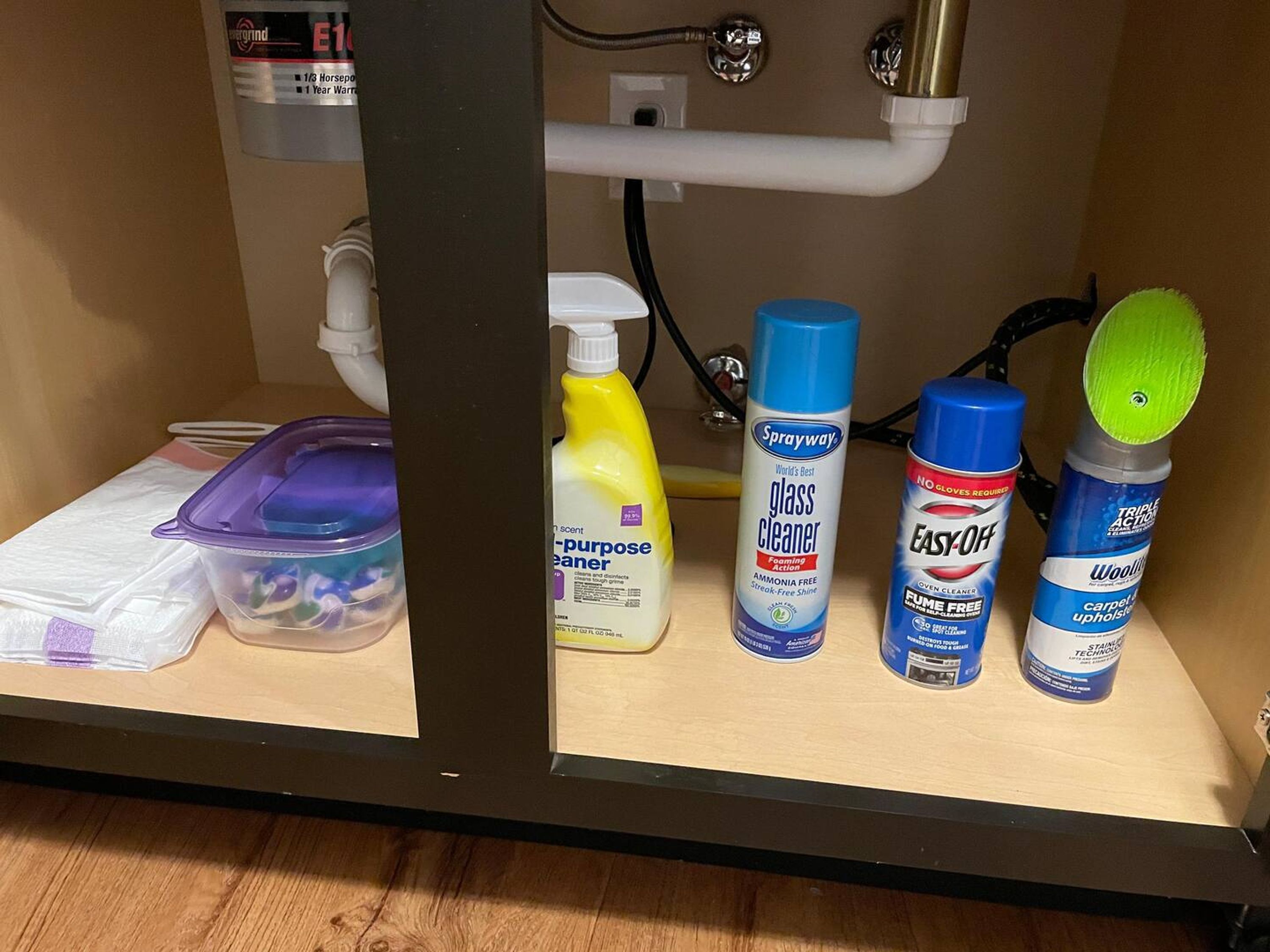 A bathroom shelf with cleaning supplies including glass cleaner, oven cleaner, and a brush.