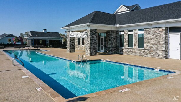 A pool area with a stone building labeled "NOW LEASING" and a clear blue sky.