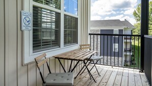 A covered outdoor seating area with a table and chairs, a no-smoking sign, and a view of a building in the background.
