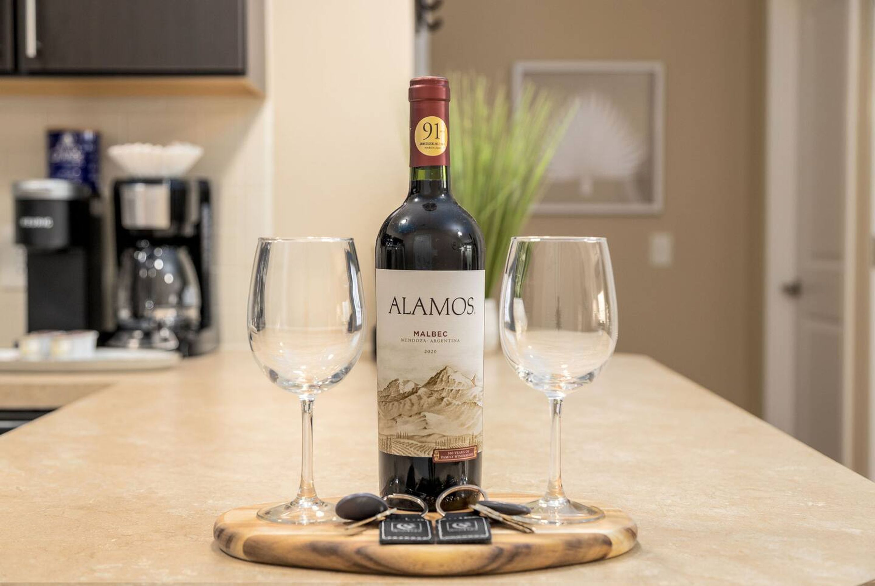 Une bouteille de vin Alamos posée sur une planche en bois, accompagnée de deux verres et d’un trousseau de clés.