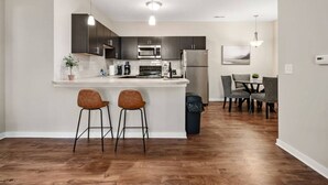 A modern kitchen with dark cabinets, a stainless steel refrigerator, and a bar area with two stools.