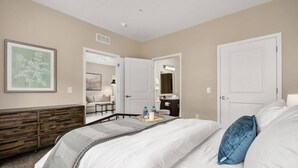 A hotel room with a large bed, a dresser, a mirror, and a door leading to a bathroom.