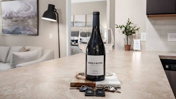 A kitchen counter with a wine bottle labeled "BREAD & BUTTER Pinot Noir 2022," a wine glass, and a set of keys.