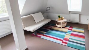 A modern room with a sofa, a small round table, a colorful striped rug, a lamp, and a window with blinds. - Apartment 'Ferienwohnung Für Max 2 Personen' (Hannover)