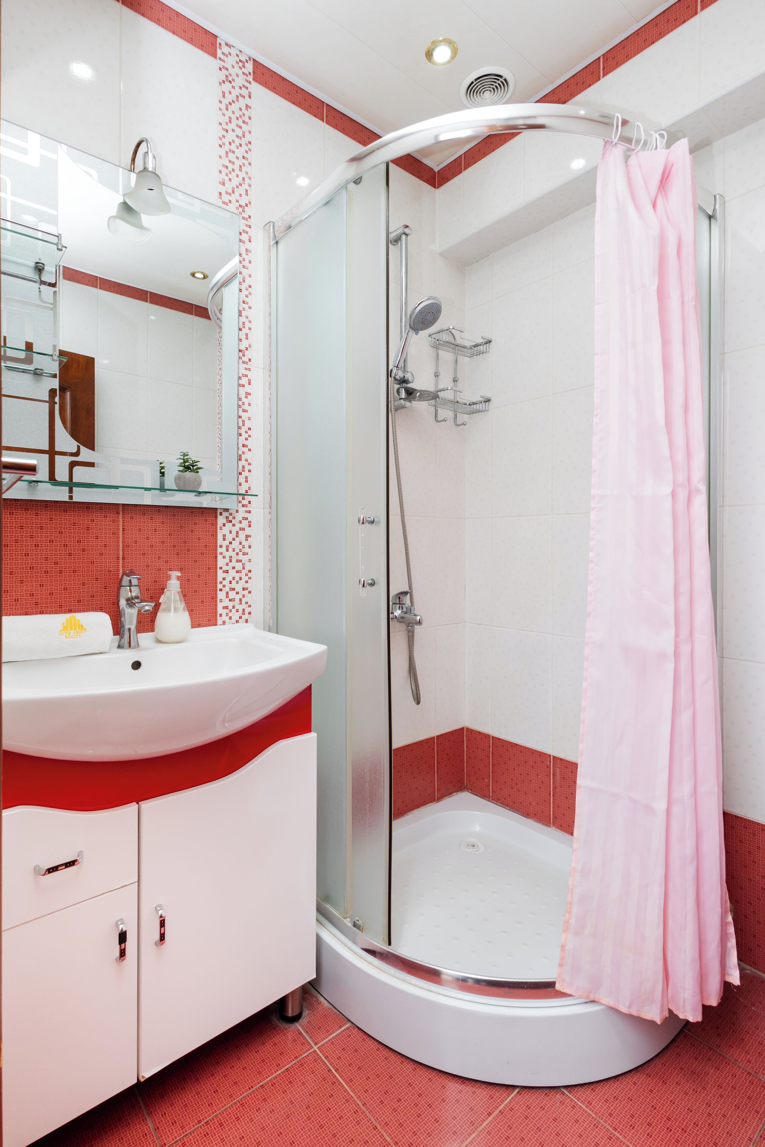 Ein modernes Badezimmer mit einer ein Glasfachwerk-Dusche, einem weißen Waschbecken mit rotem Akzent und einem Spiegel über dem Waschbecken.