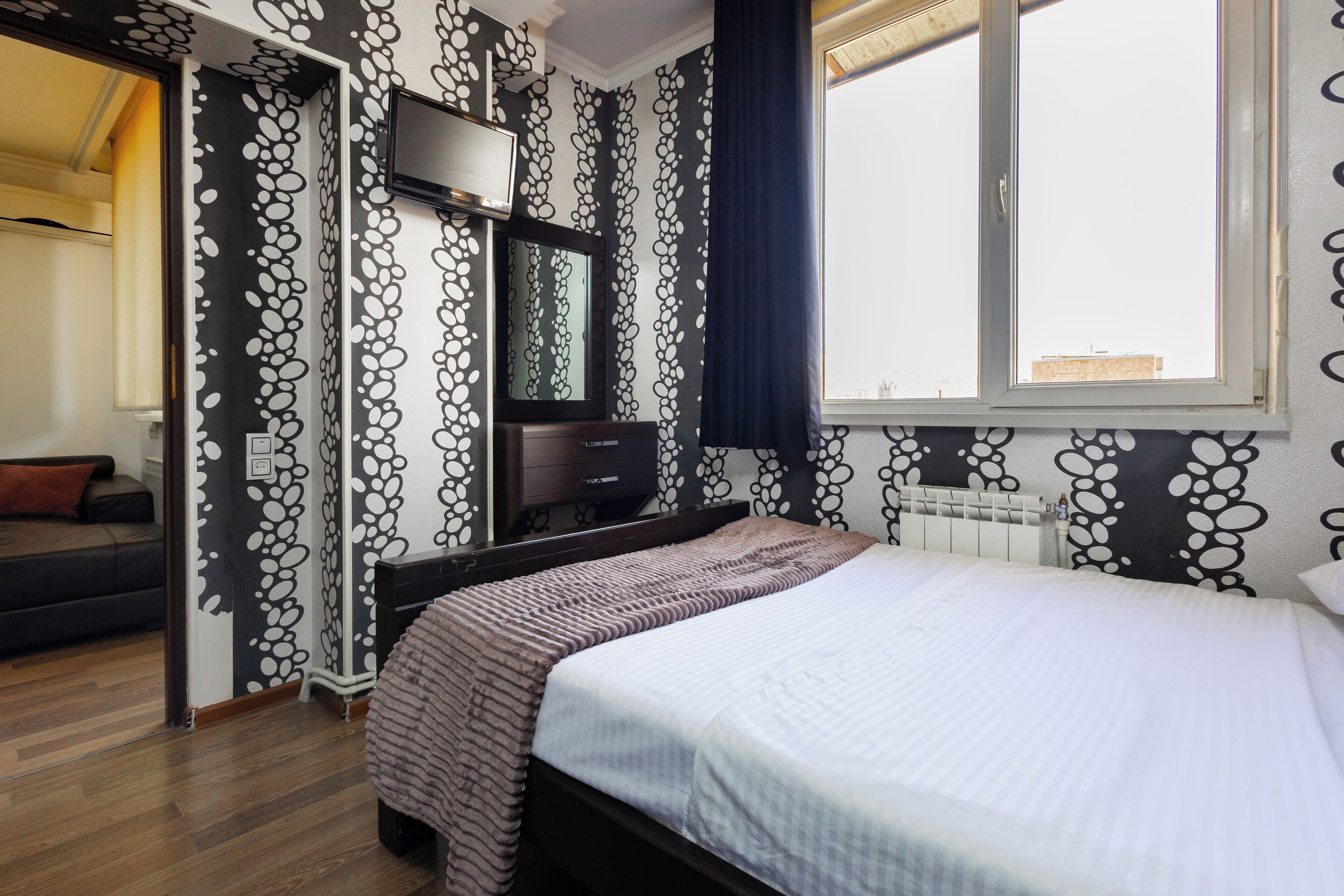 A bedroom with a bed, a TV mounted on the wall, and a window with curtains.