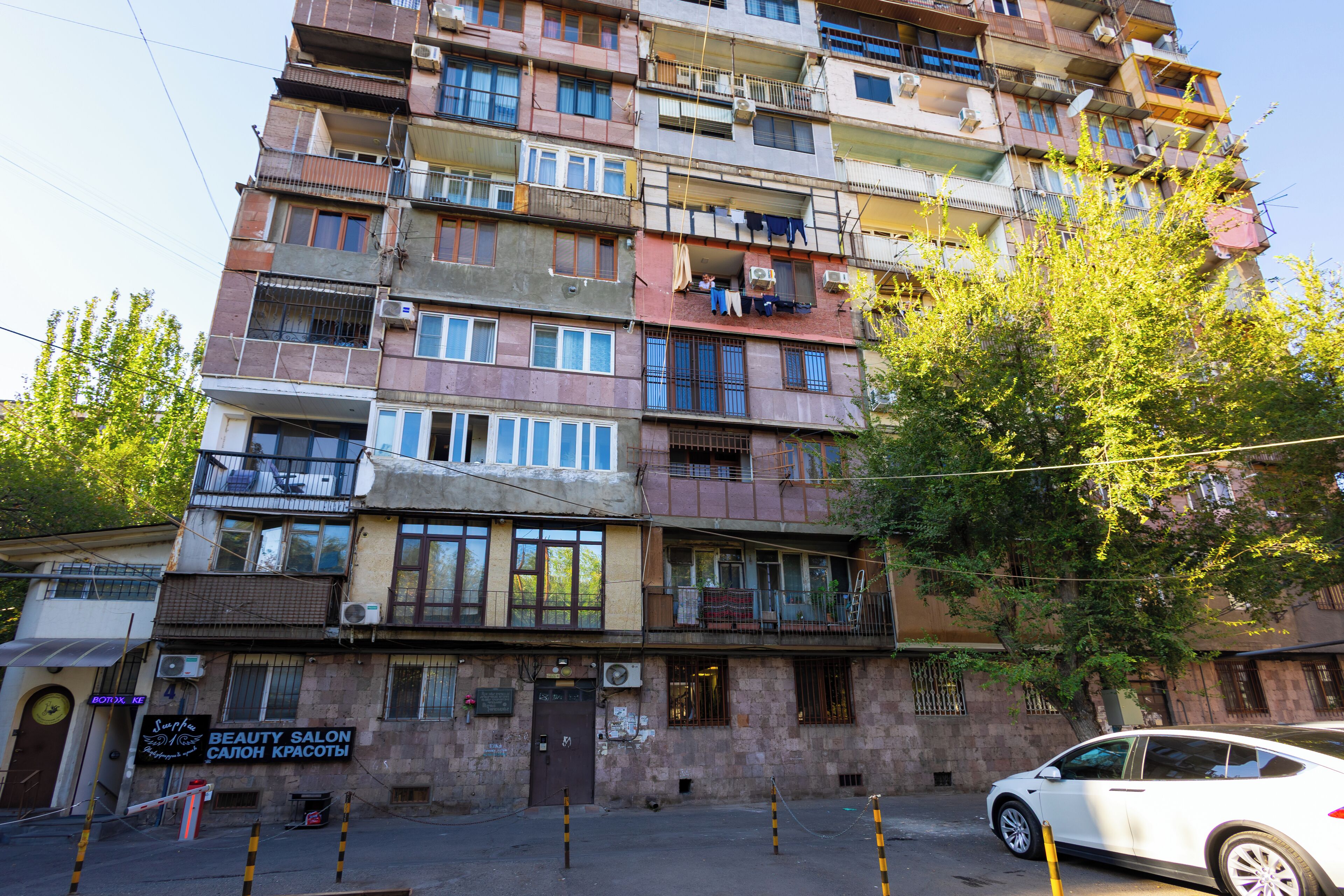 A multi-story building with balconies, a visible storefront with a sign for a beauty salon, and a parked car.