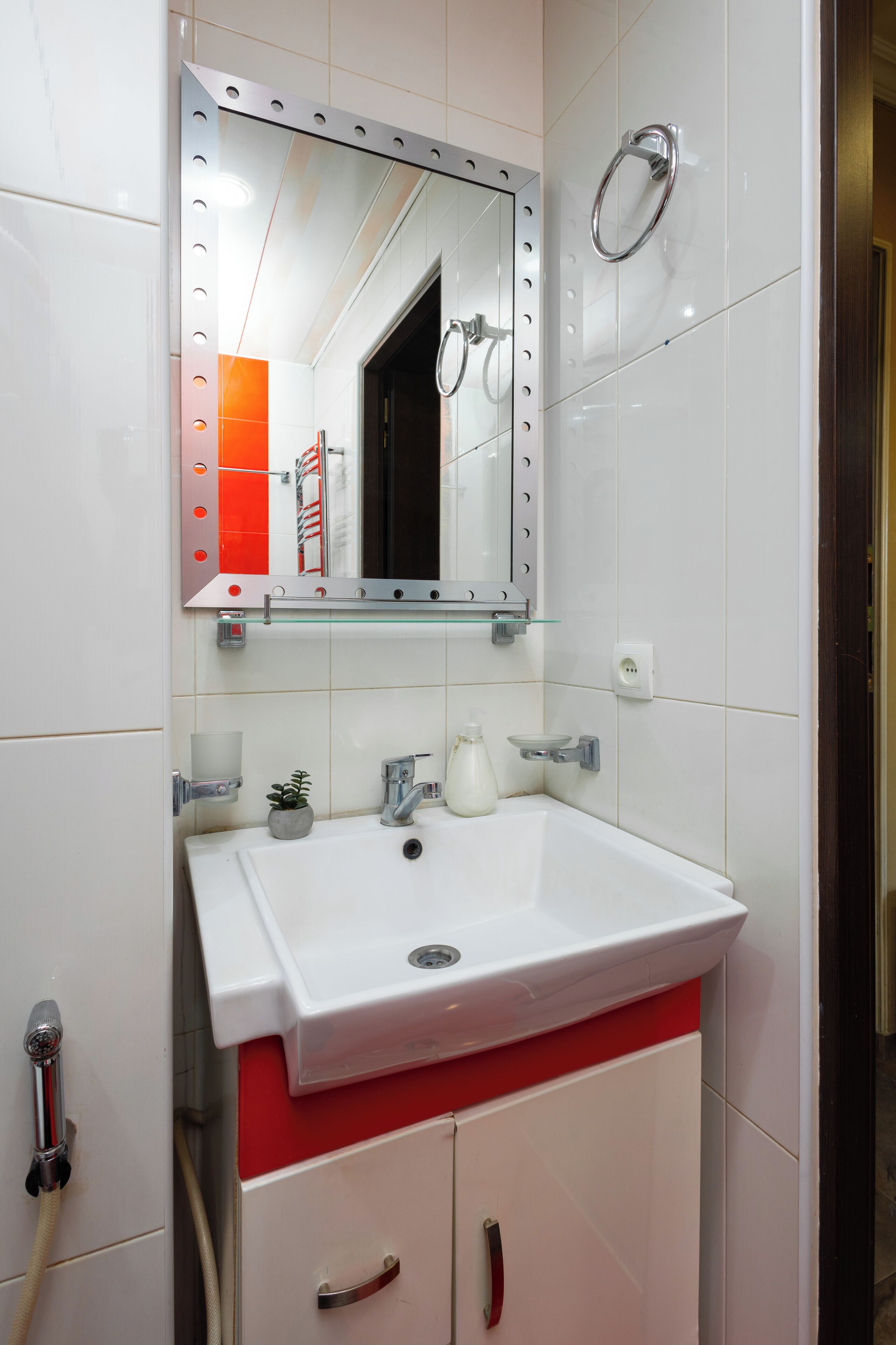 A bathroom with a white sink, red cabinet, and a mirror with lights.