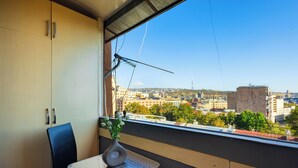 A room with a view of a cityscape, a table with a vase, and a chair.