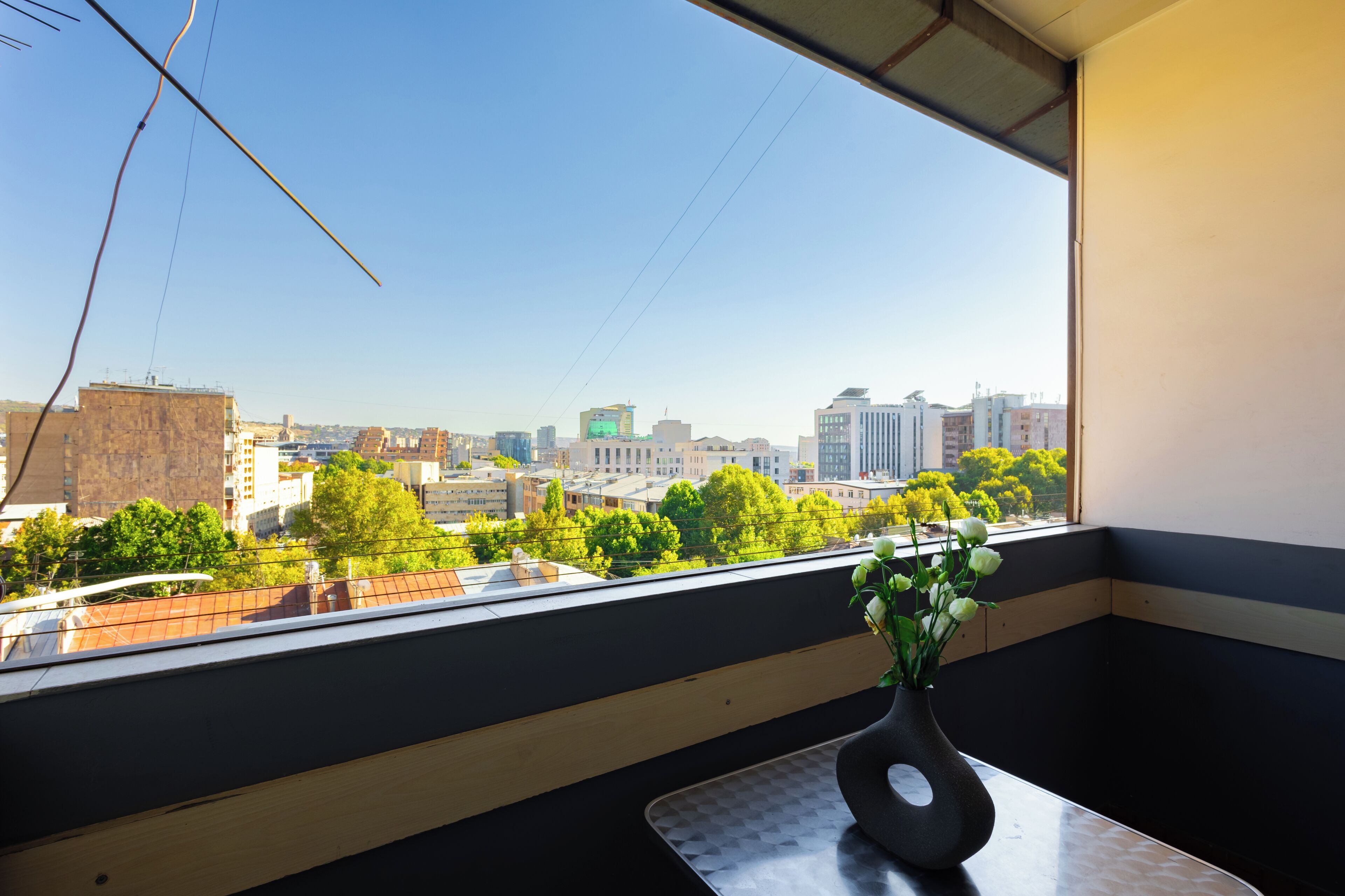 A room with a view of a cityscape through a window, a vase with flowers on a table, and a checkered floor.
