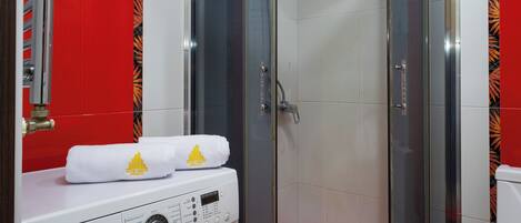 Uma casa de banho compacta com chuveiro em cabine de vidro, máquina de lavar e sanita.