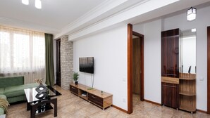 A modern living room with a green sofa, a glass coffee table, a TV, and a wooden cabinet.