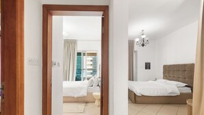 A hotel room with a bed, a bedside table, a chandelier, and a view of the outside. - Diamond 6 Residences by CEG Group (Dubai)