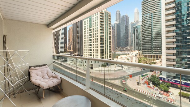 A balcony with a view of a cityscape, a cushioned chair, and a metal drying rack. - Diamond 6 Residences by CEG Group (Dubai)