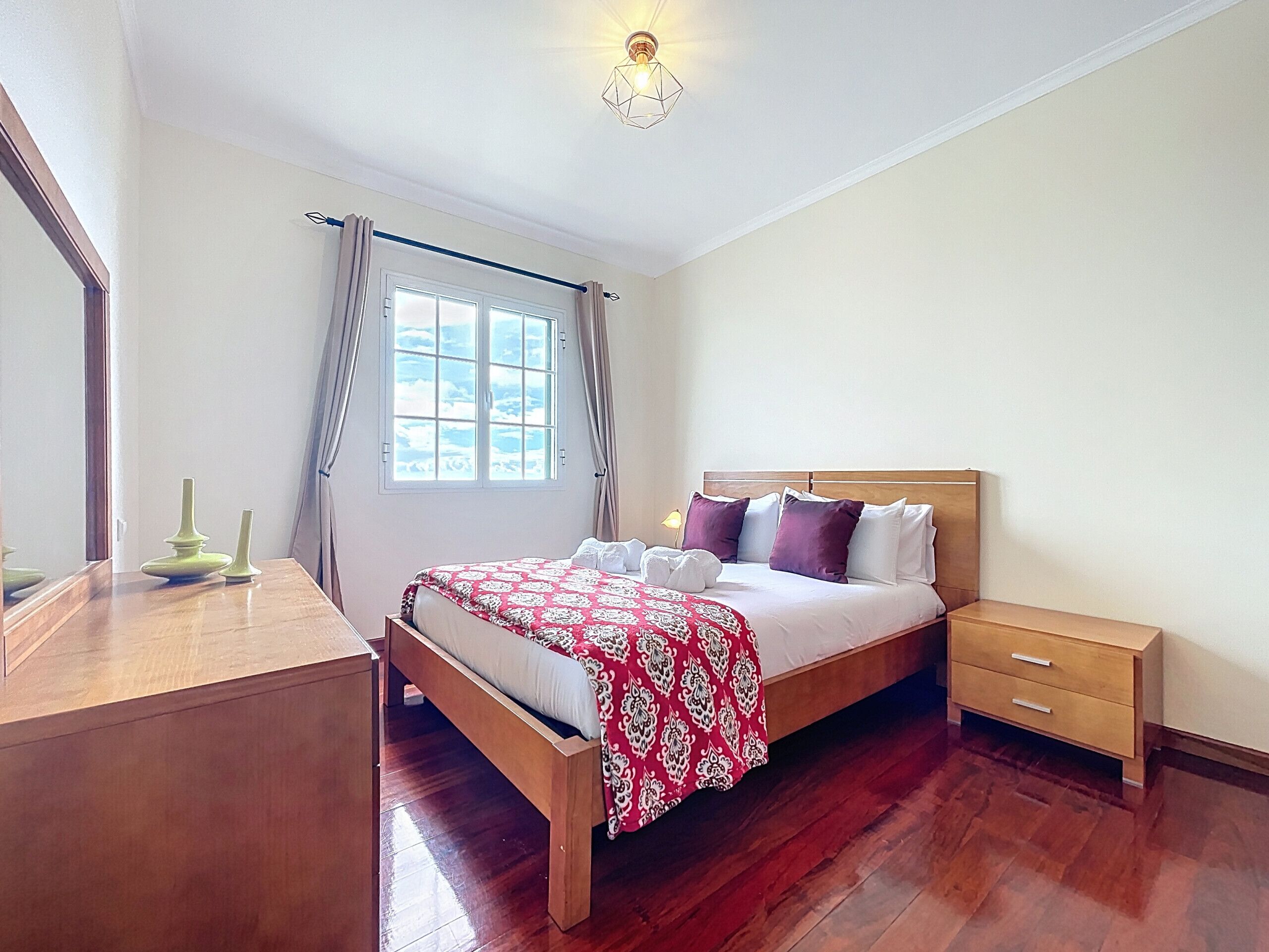 A bedroom with a wooden bed, a nightstand, a desk, and a window with curtains.