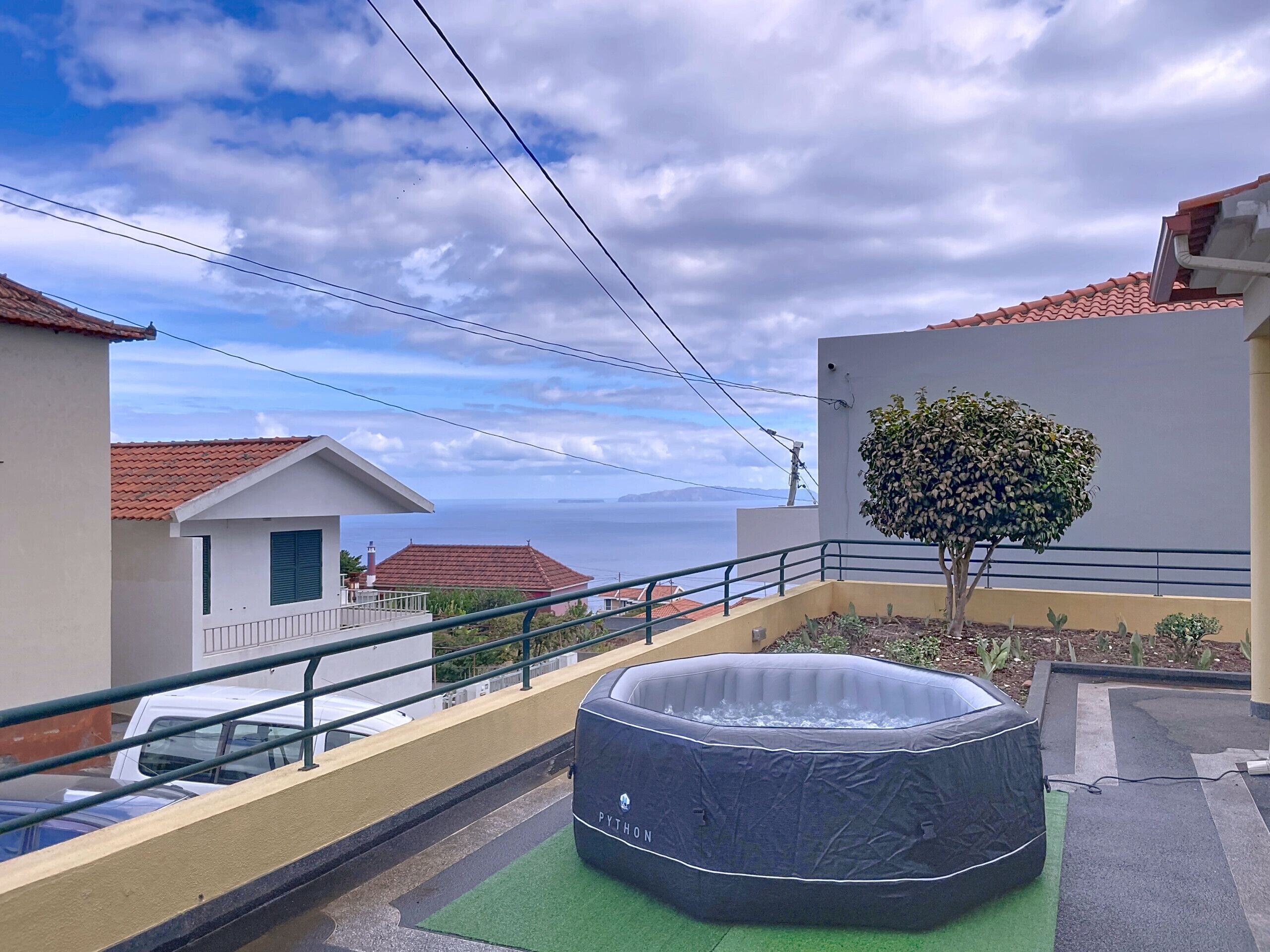A rooftop with a hot tub, a small tree, and a view of the sea.