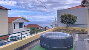 A rooftop with a hot tub, a small tree, and a view of the sea.