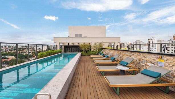 Ein Pool auf dem Dach mit Holzterrasse, Liegestühlen und Blick auf die Stadt.