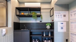 Eine moderne Küche mit schwarzen Arbeitsplatten, grauen Schränken und einer eingebauten Ablage mit Pflanzen. Unter der Arbeitsplatte befinden sich Körbe und an der Wand ist ein QR-Code angebracht.