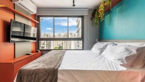 Ein modernes Schlafzimmer mit großem Fenster, Flachbildfernseher und einem Bett mit weißen Leinen.
