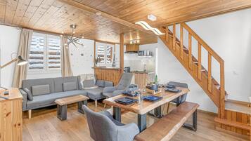 A cozy living area with a wooden ceiling, a sofa, a dining table with benches, and a staircase.
