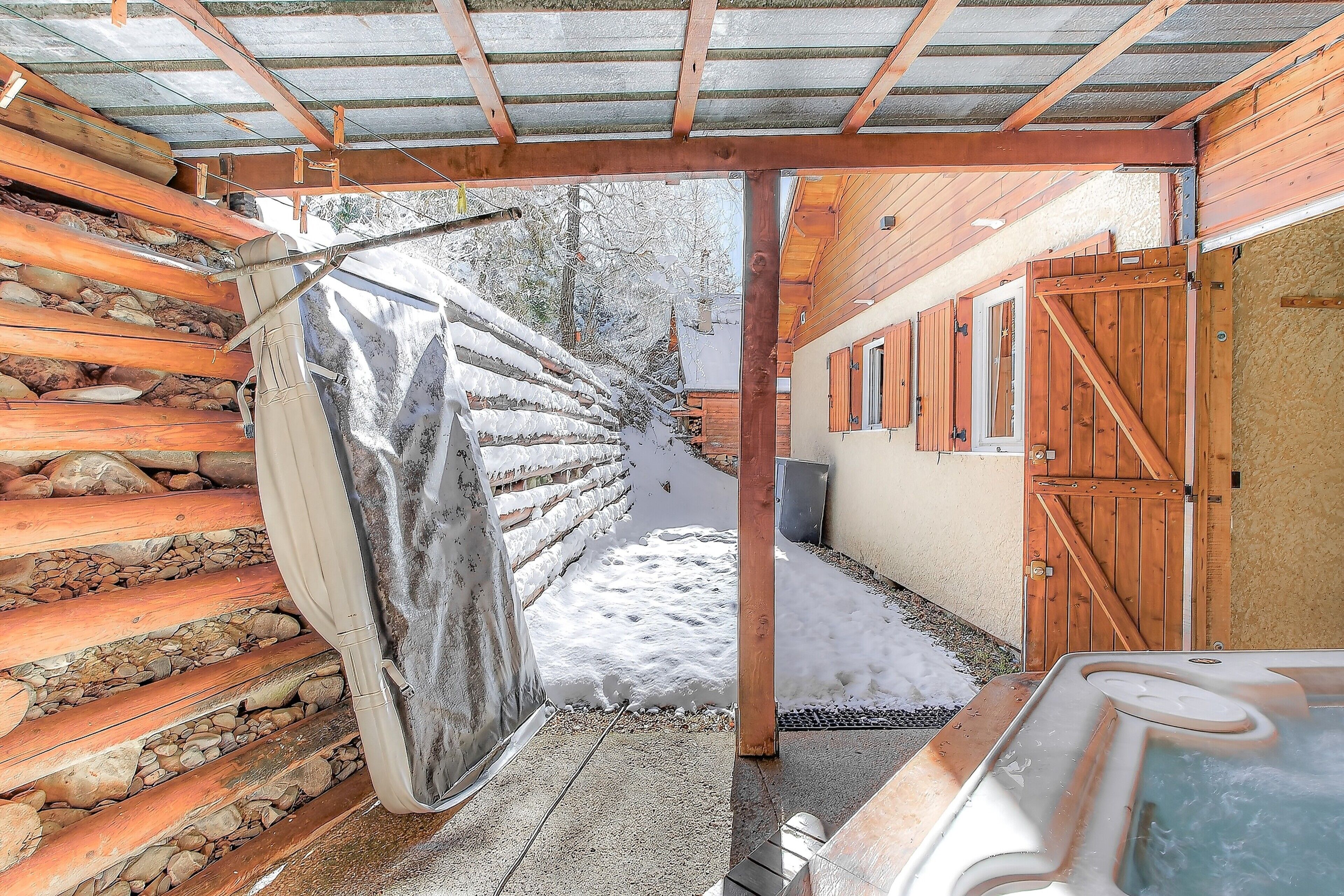 Una cabaña de madera con jacuzzi, una verja de madera y un sendero cubierto de nieve.