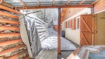 Una cabaña de madera con jacuzzi, una verja de madera y un sendero cubierto de nieve.