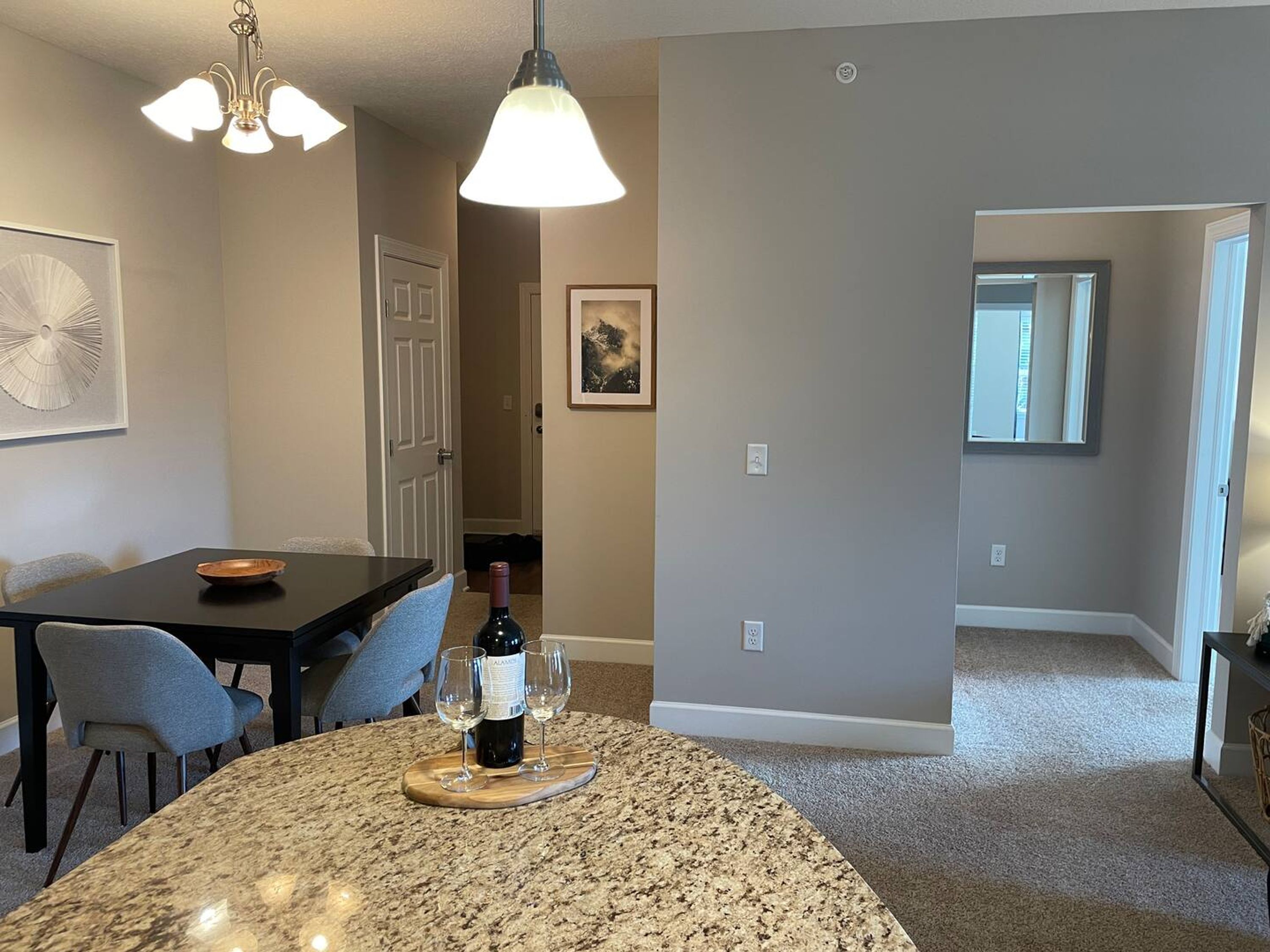 A dining area with a granite island, two chairs, a table, and a bottle of wine on a coaster.