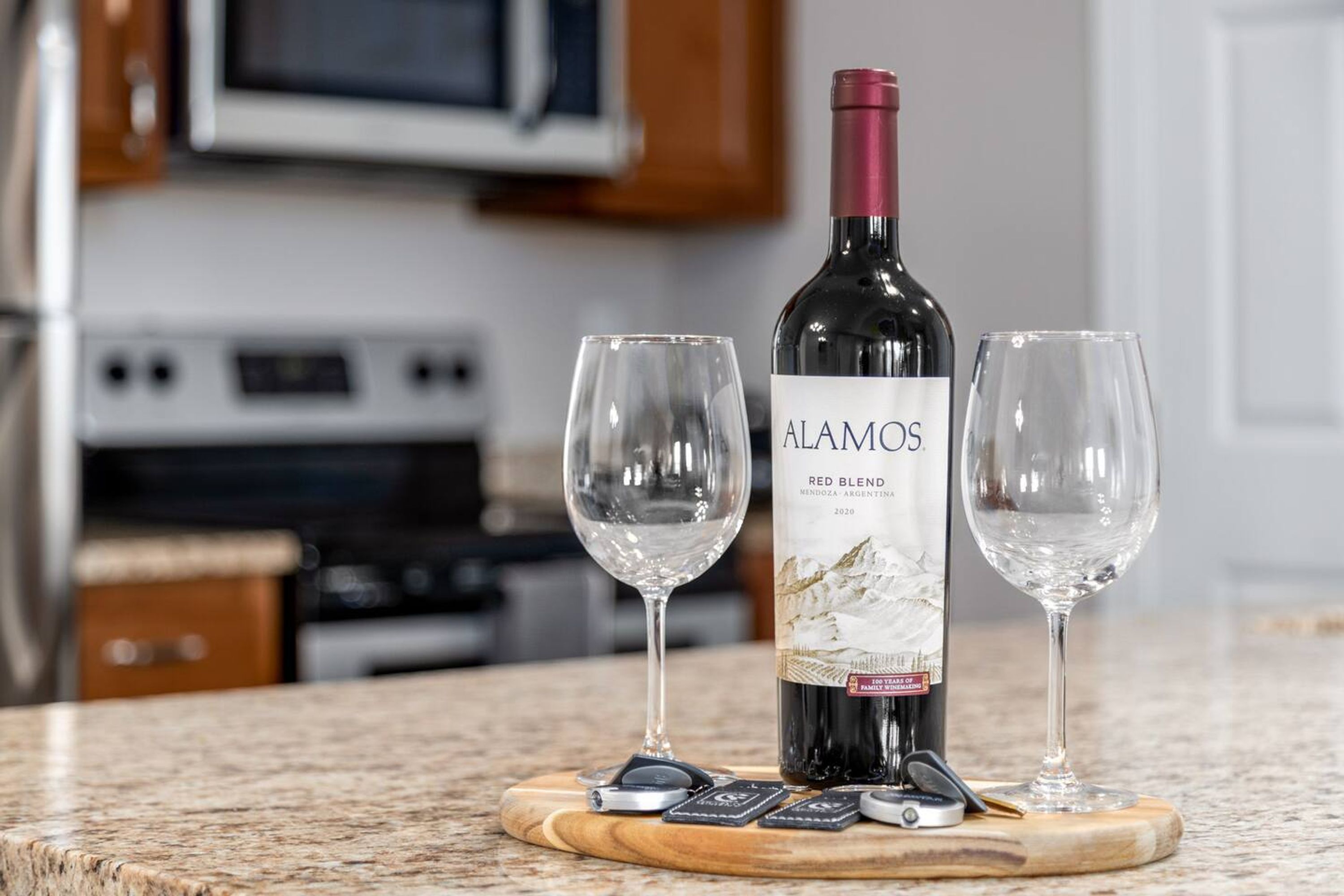 A bottle of Alamos Red Blend wine on a wooden coaster with two glasses beside it.