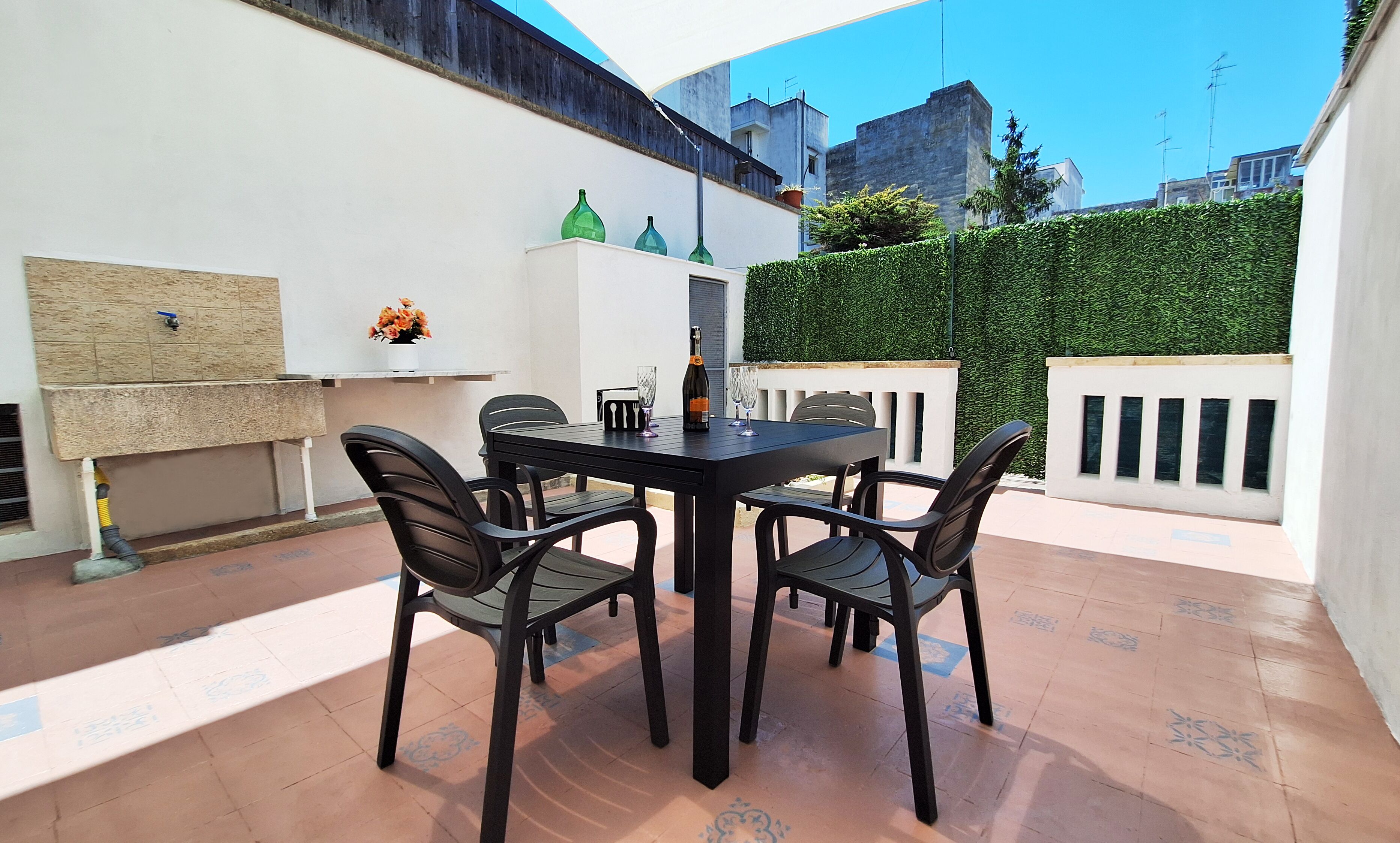Un patio con tavolo e sedie, una bottiglia di vino e un vaso di fiori.