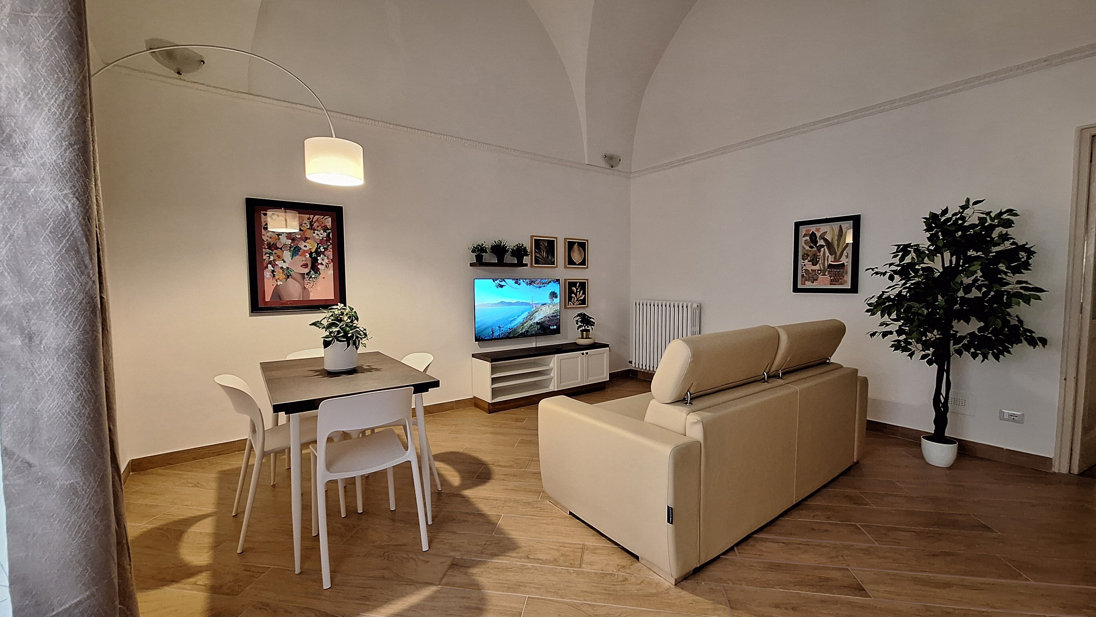 Un soggiorno con divano, televisione, tavolo da pranzo con sedie e una pianta in vaso.