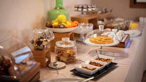Una mesa de buffet con diversos alimentos, incluyendo un tarro de galletas, un plato de frutas y un pastel cubierto.