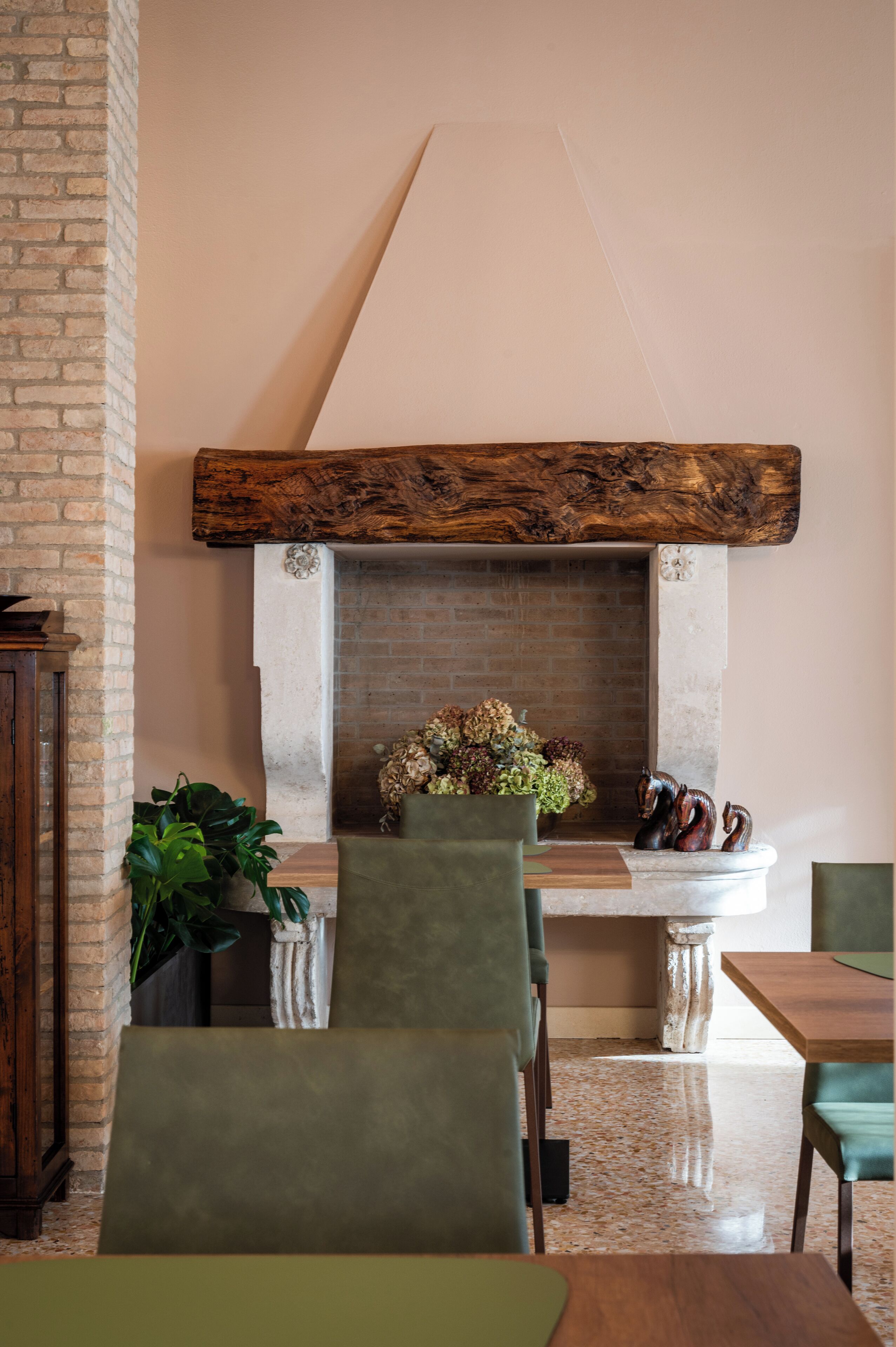 A dining area with a brick wall, a fireplace with a stone surround, and green upholstered chairs.