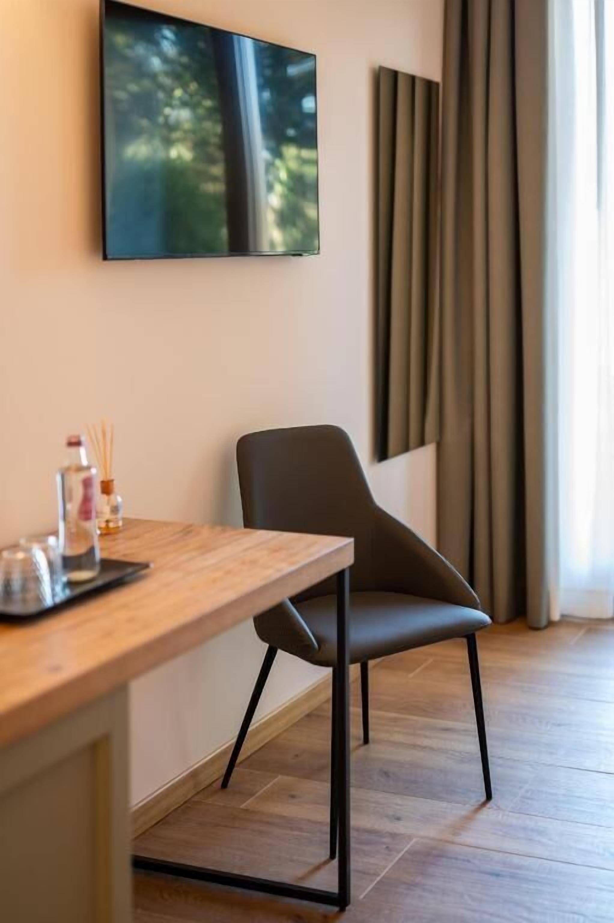 Een moderne kamer met een houten bureau, een stoel, een tv aan de muur en een raam met gordijnen.
