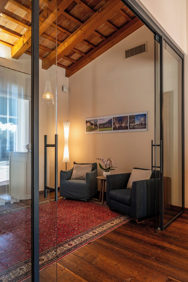 A modern living room with a wooden ceiling, a red patterned rug, two grey sofas, a small table with a vase, and a wall with framed pictures. - Aura - Dimore ad Arquà Petrarca (Arquà Petrarca)
