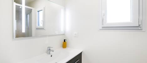 A bathroom with a white sink, a mirror, a window, and a yellow bottle.