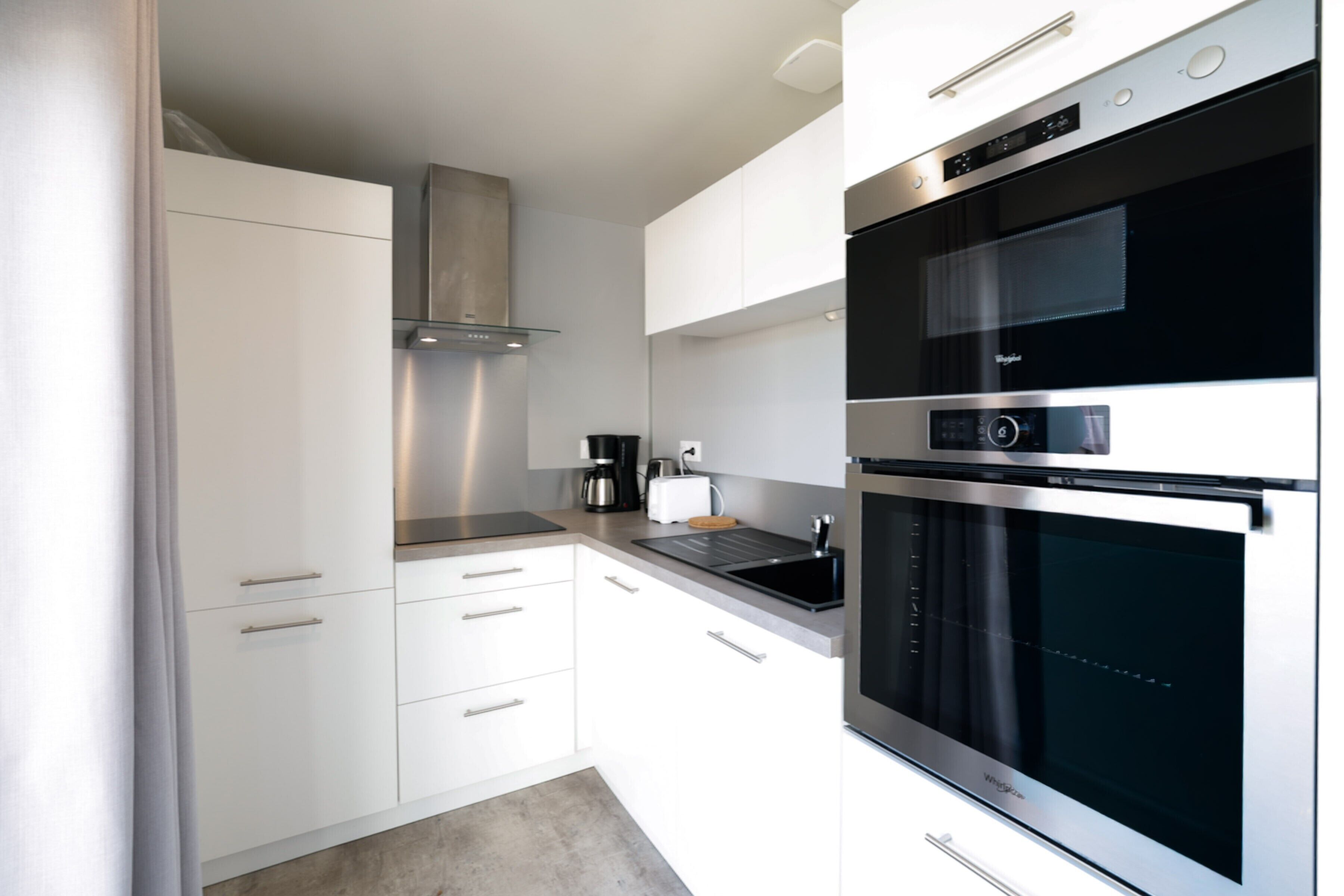 A modern kitchen with white cabinetry, stainless steel appliances, and a built-in oven.