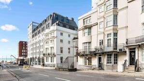A street view with a mix of modern and traditional buildings, including a corner building with a balcony and a building with a black awning. - Starfish Studio By My Getaways (Brighton)