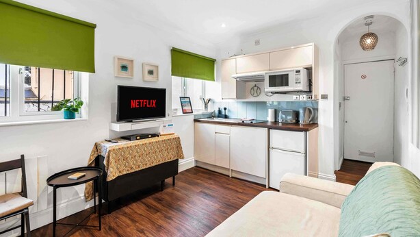 A compact living space with a kitchenette, a dining area, and a seating area with a television displaying 'NETFLIX'. - Starfish Studio By My Getaways (Brighton)