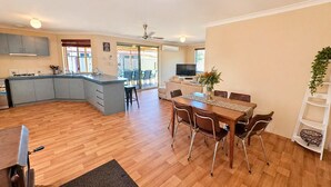 Une cuisine moderne avec un îlot central, un coin repas avec une table et des chaises en bois, un téléviseur et une petite plante.